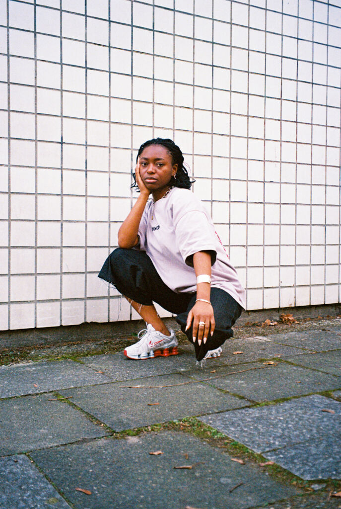 Die DJ Josiane kniet vor einer Kachelwand und schaut in die Kamera